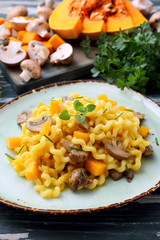 pasta maccheroni con zucca gialla e funghi su tavolo di cucina verde rustico