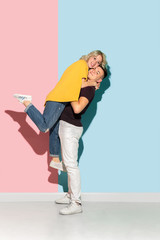 Young emotional man and woman in bright casual clothes posing on pink and blue background. Concept of human emotions, facial expession, relations, ad. Beautiful caucasian couple hugging and cuddling.