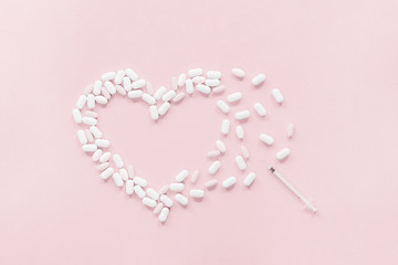 White and pastel pink tablets pills forming heart shape with syringe on pink. Female health risks