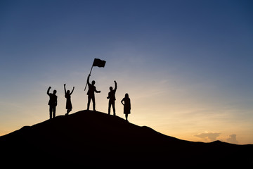 Silhouette of people are celebrating success at the top of the mountain, sky and sun light background. Team business concept.