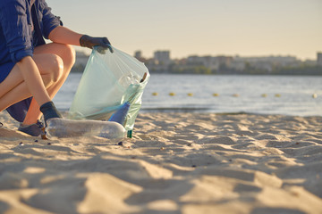 Young volunteer in black gloves is walking with garbage bag along a dirty beach of the river and...