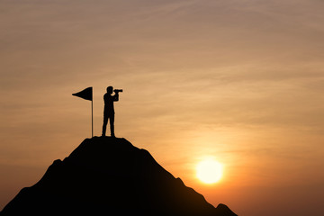 Silhouette of businessman on top of mountain at sunset background. Vision concept.