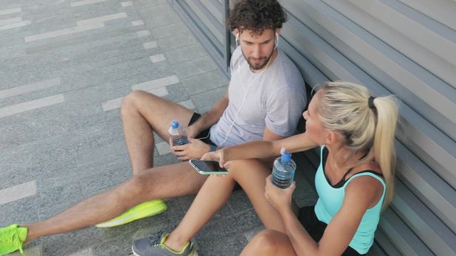 Modern woman and man jogging / exercising in urban surroundings and using cellphone at a pause / break.
