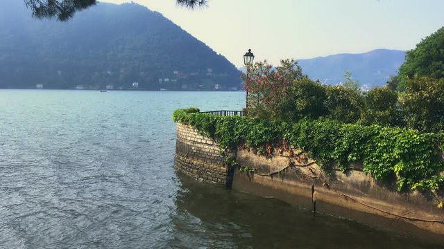 view on the shore of como Lake in the village of Cernobbio with a brick wall and lush garden