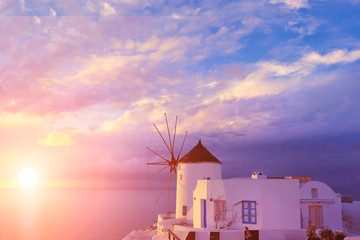 Traditional white windmill in Oia village on Santorini, Greece, on sunset with Sun setting through dramatic heavy clouds