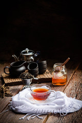 Hot tea in a glass teapot and tea cup with a jar of honey on a black background