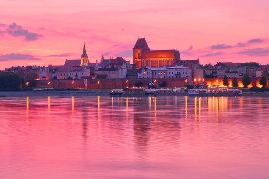 Torun old town in Poland, UNESCO world heritage site, with illumination, reflected in Vistula river on pink sunset.