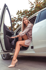 Beautiful girl business lady, in summer in autumn city, gets out of car. A strict suit tanned...