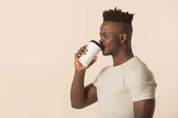handsome young african man on a beige background with a glass of coffee in his hands