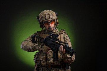Fototapeta premium a male soldier in military clothes with a weapon on a dark background