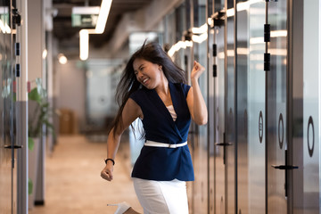 Excited Asian businesswoman celebrating success, dancing in office hallway
