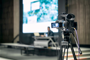 The back view of a professional digital video camera is recording video a presentation event.
