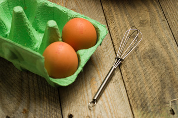 Eggs and whisk  on wooden background