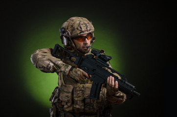 Fototapeta premium a male soldier in military clothes with a weapon on a dark background