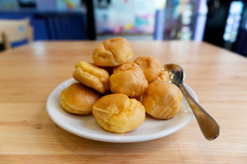 Cream puffs or eclair or choux cream with vanilla custard on wooden table on white plate put on wood table , eat to tea and coffee with cocoa cold, copy space
