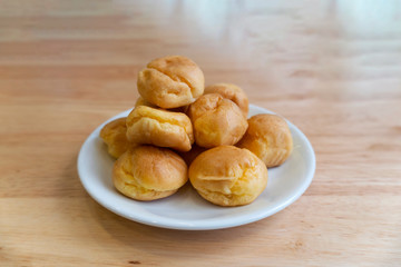 Cream puffs or eclair or choux cream with vanilla custard on wooden table on white plate put on wood table , eat to tea and coffee with cocoa cold, copy space