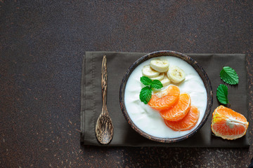 Greek yogurt with orange and a banana mint in a rustic bowl on on rusty metal wall , food and healthy meal concept, top view, copy space.