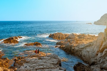 Landscape with sea and couple on a rocky coast at sunset