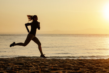 Fototapeta na wymiar Dedicated female runner jogging at the beach at sunrise.