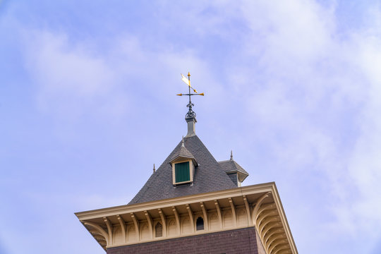 Weather vane with cross and lightning rod located on top of a needle on the black slate roof of an attic