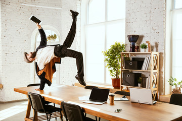 Young caucasian businessman having fun dancing break dance in the modern office at work time with gadgets. Management, freedom, professional occupation, alternative way of working. Loves his job.