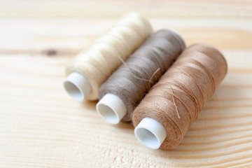 Fototapeta na wymiar Three bobbins of threads of brown shades lie on a wooden background