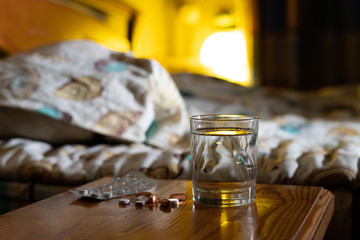 some of medicine pills and a glass of water  on a nightstand next to the bed at night, treatment insomnia concept