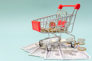 red shopping cart with gold and silver coins stands on dollar bills on a blue background. The concept of online shopping, online shopping