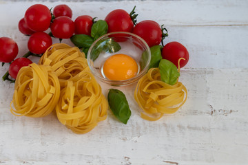 Ingredients for cooking Italian pasta. Pasta, basil, cheese, cherry tomatoes, olive oil, egg, yolk. On a dark background. Copy space.