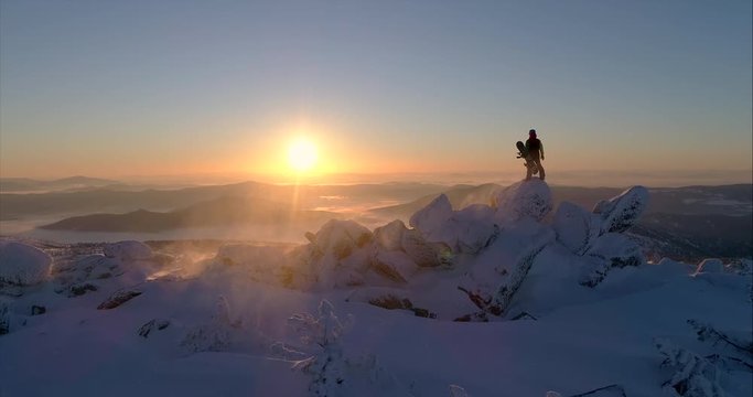 Aerial view. Freerider stands on top of the mountain, snowboard in hand. movable camera plans. Fresh powder. Extreme freeride skiers skiing from the top. beautiful storm of snow flying in the frame