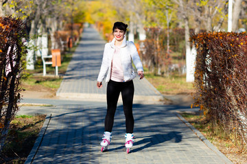 Fototapeta premium A young woman in white jacket trousers skates for the first time. Girl learns to skate, sunny day