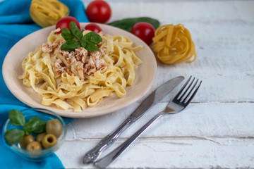Italian pasta, spaghetti with avocado, basil, cream, cheese. Cherry tomatoes, olive oil. Meat with noodles. On a gray background. In the background is a glass of orange wine. Copy space. 