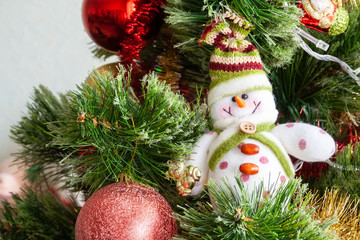 Green artificial Christmas tree decorated with beautiful smiling textile snowman, red balls and other toys. Home decoration for a family holiday. Selective focus