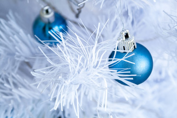 Closeup view of a blue matte ball hanging on a silver thread on a white artificial Christmas tree...