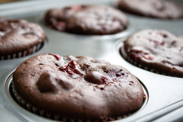 Closeup view on baked chocolate muffins with cherries in teflon baking dish. Selective focus