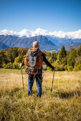 A man traveler with a backpack stands on a hill of beautiful alpine landscape