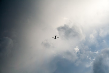 A small black silhouette of a flying airplane against a dramatic cloudy dark blue sky. Thunderstorm flights. Non-flying weather