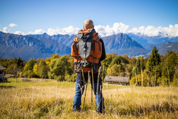 A man traveler with a backpack stands on a hill of beautiful alpine landscape