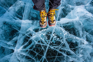 Traveller man foot standing on cracks surface of the natural ice in frozen water at Olkhon Island,...