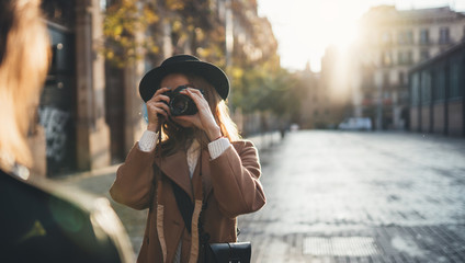 Sunlight flare street in europe city. Photographer in glasses with retro camera take photo model girlfriend. Tourist smiling girl in hat travels in Barcelona holiday. Photoshoot concept