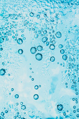 transparent background of soda water and ice with bright blue bubbles within the glass