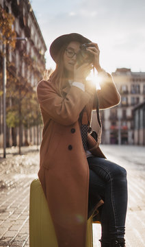Photographer tourist with suitcase take photo camera. Trip concept. Girl in hat travels in Barcelona. Sunlight flare street in europe city. Traveler hipster shooting architecture, copy space mockup