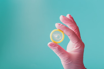 An opened condom in a hand in a pink glove holds on a blue background. Latex for protection against pregnancy.