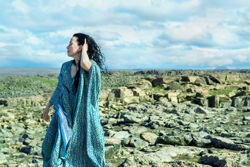 Women in a blue dress fluttering in a wind standing on a lava rocks field pn west Iceland © Olena Ilienko