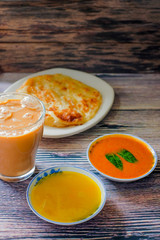 A cup of hot coffee , Roti canai or Roti Parata , dalca and curry sauce on wood background