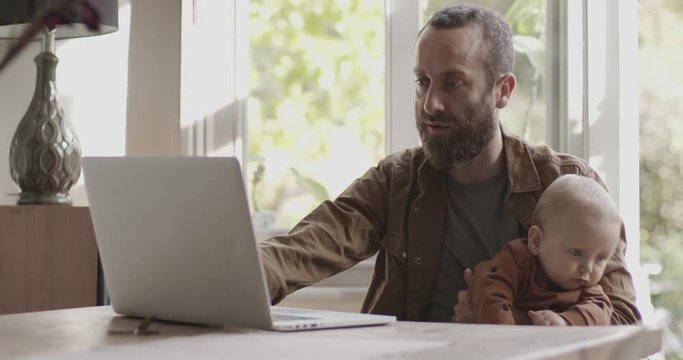 Single father working from home on laptop and looking after baby son