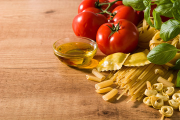 Italian pasta and ingredients. Ravioli, penne pasta, spaghetti, tortellini, tomatoes and basil on wooden table