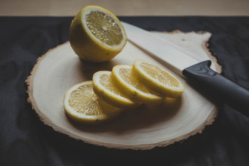 Halved lemon with slices on a wooden cutting board with knife on a black background