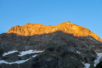 Fototapeta premium First sunbeams of the day toughing the massive, sharp stony mountain range of Schladming Alps, Austria. The mountain is partially overgrown with green bushes. Dangerous mountain climbing.