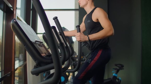 Portrait fitness man warm up before training on elliptical cross trainer in gym club. Close-up male training cardio exercise on cross trainer in fitness.